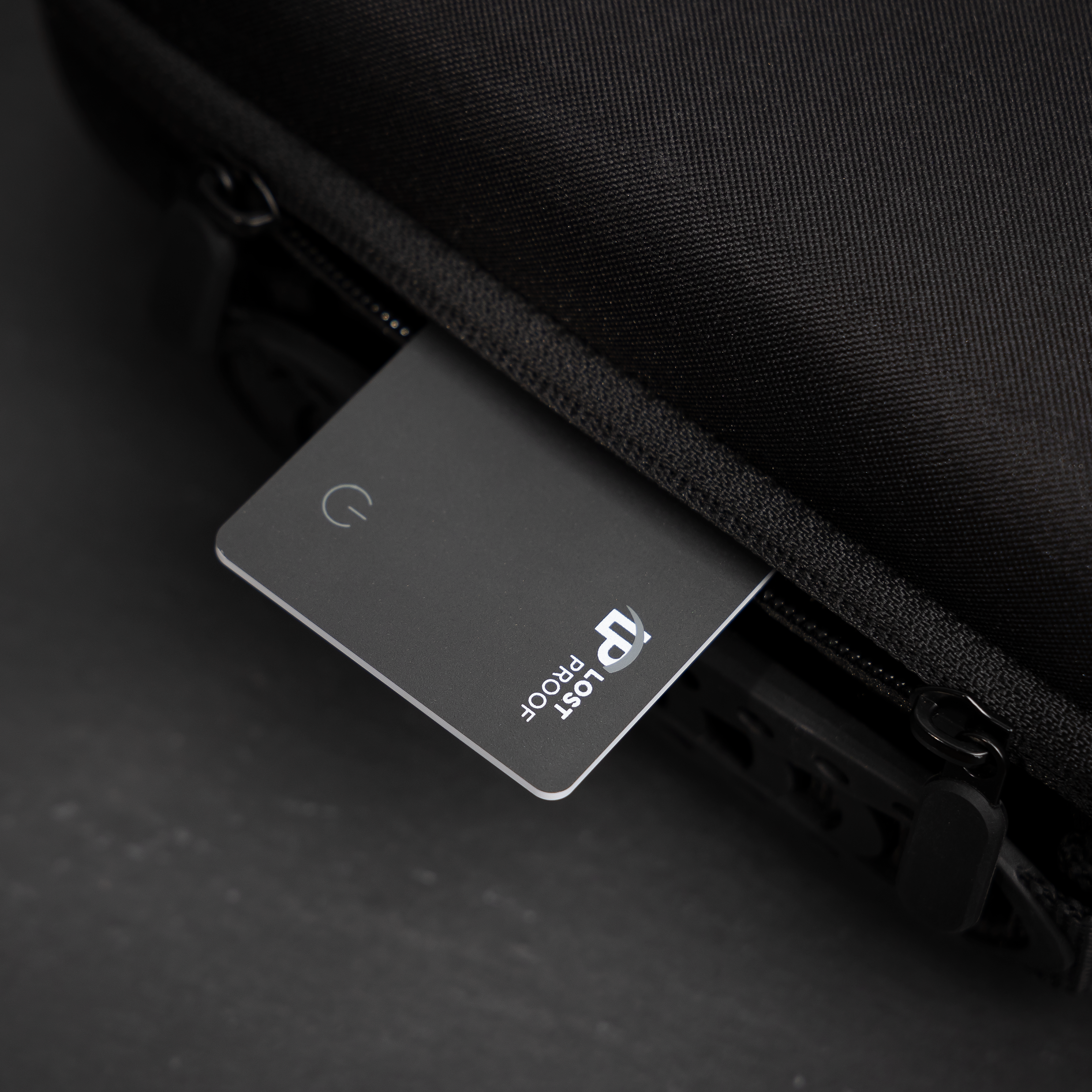 A sleek black LostProof CardTrack GPS tracker partially inserted into a black travel bag's zippered compartment, showcasing its slim design and discreet fit. The ultimate wallet finder card that pairs seamlessly to your apple device.