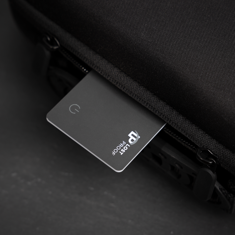 A sleek black LostProof CardTrack GPS tracker partially inserted into a black travel bag's zippered compartment, showcasing its slim design and discreet fit. The ultimate wallet finder card that pairs seamlessly to your apple device.